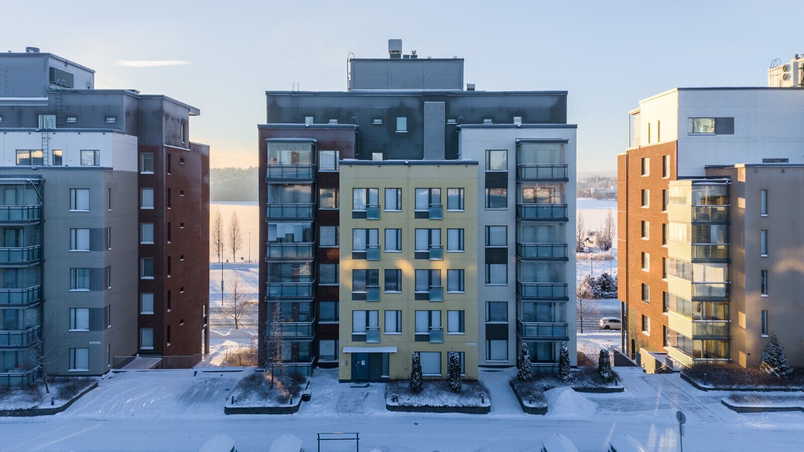 A multi-story residential building with a modern architectural design, featuring a mix of glass and brick facades, and a central courtyard with snow-covered ground.