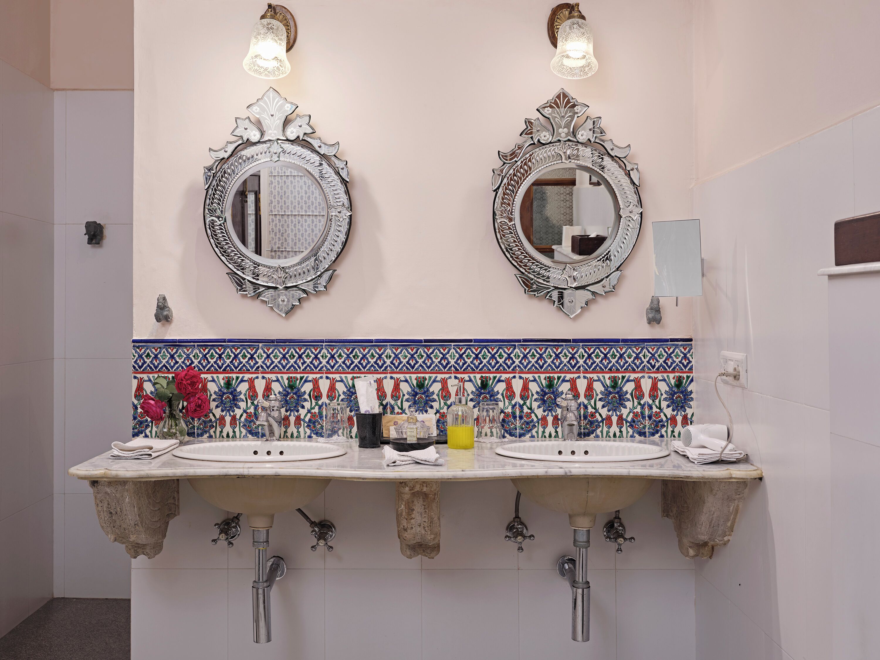 A bathroom with two sinks, ornate mirrors, and a decorative tile backsplash.