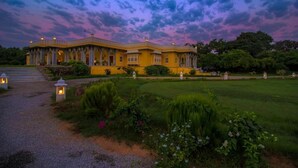 A large, yellow building with a symmetrical facade and multiple windows, surrounded by a well-maintained garden with pathways and lanterns. - Dev Shree Deogarh (Devgarh)