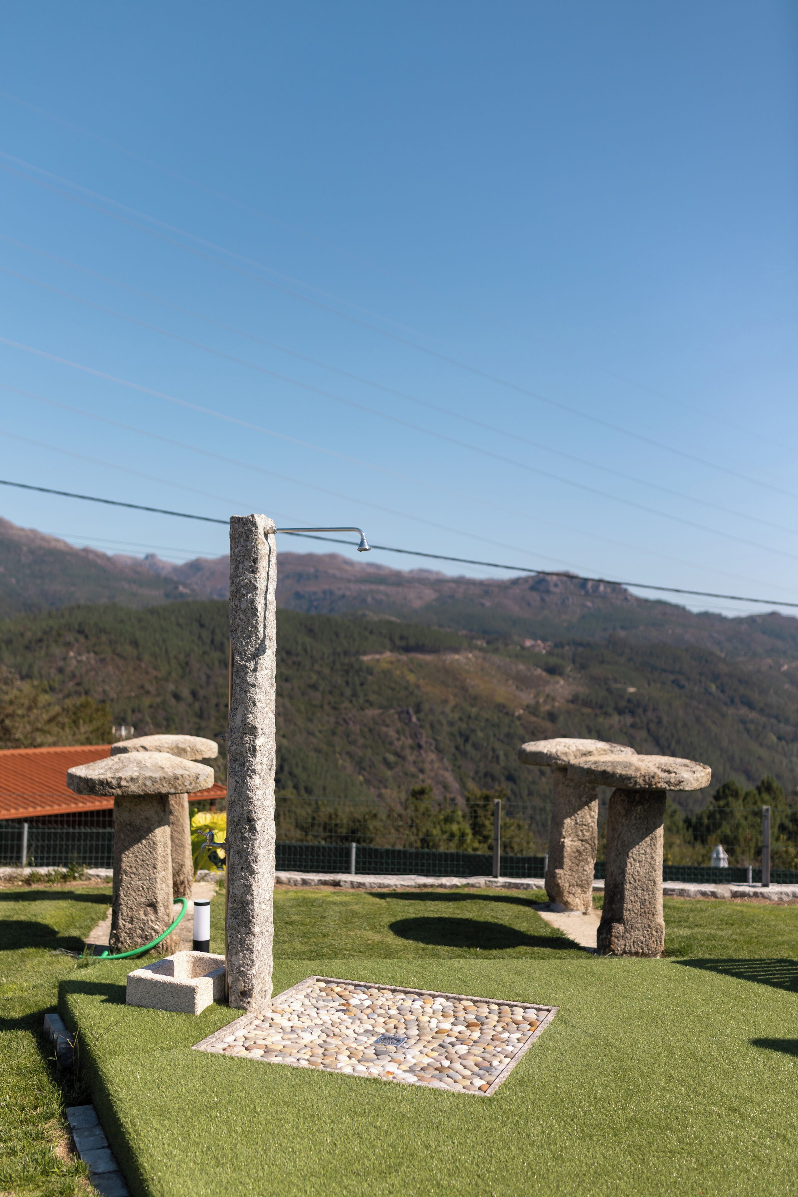 A stone structure with a metal fixture on a grassy area with a stone base, surrounded by mountains.