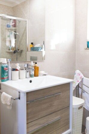 Uma casa de banho com uma pia branca, um espelho e produtos de higiene no balcão.
