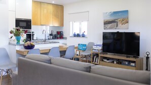 Ett modernt vardagsrum med en grå soffa, en tv och en matplats med ett träbord och stolar.