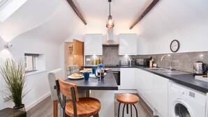 Una cucina moderna con mobili bianchi, un piano di lavoro nero e un lampadario a sospensione. C'è un'area pranzo con tavolo e sedie, e una lavatrice nell'angolo.