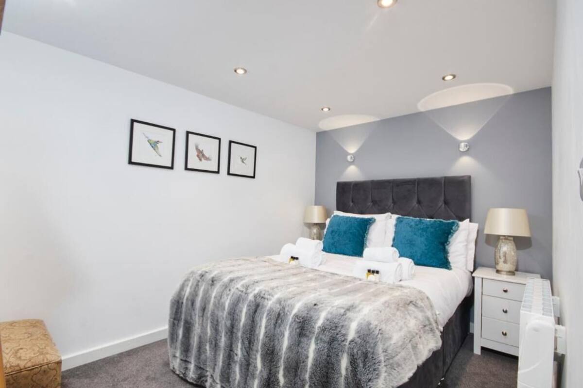 Un dormitorio moderno con una cama tapizada en gris, mesitas de noche blancas y una manta mullida gris. Hay tres cuadros en la pared y un cabecero gris.
