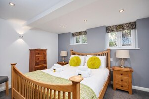 Un dormitorio con una cama de madera, dos mesitas de noche con lámparas, un aparador de madera y una ventana con cortinas estampadas.