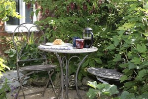 A metal table with a plate of food and a coffee pot in a garden setting.
