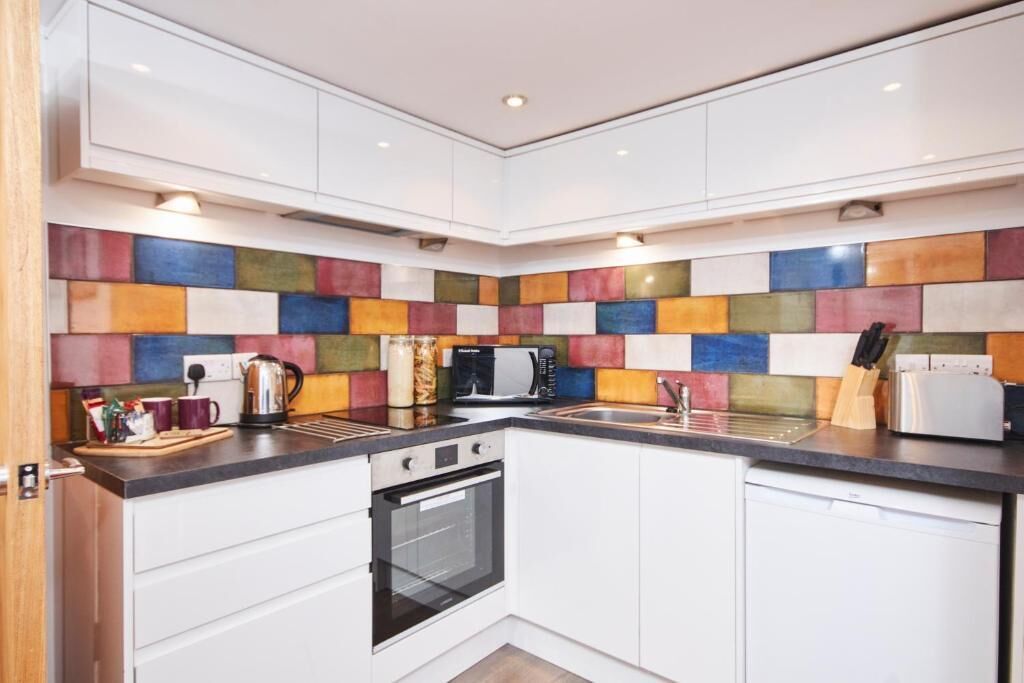 A modern kitchen with white cabinets, a colorful backsplash, a built-in oven, a microwave, a toaster, and a sink.