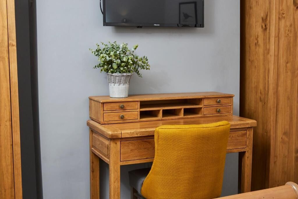 A wooden desk with drawers and a chair, a television mounted on the wall, and a potted plant on the desk.