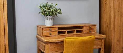 A wooden desk with drawers and a chair, a television mounted on the wall, and a potted plant on the desk.