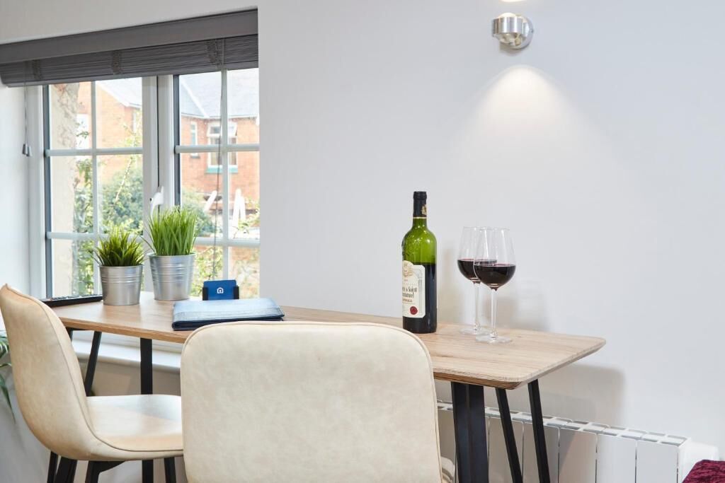 A modern room with a wooden table, two chairs, a potted plant, a bottle of wine, and a glass of wine.