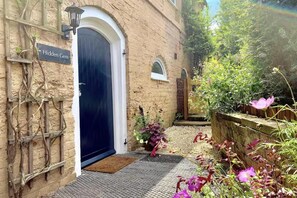 A brick building with a dark blue door, a sign reading "Hidden Gem," and a small garden with various plants and flowers. - Gateway Mews (Kegworth)