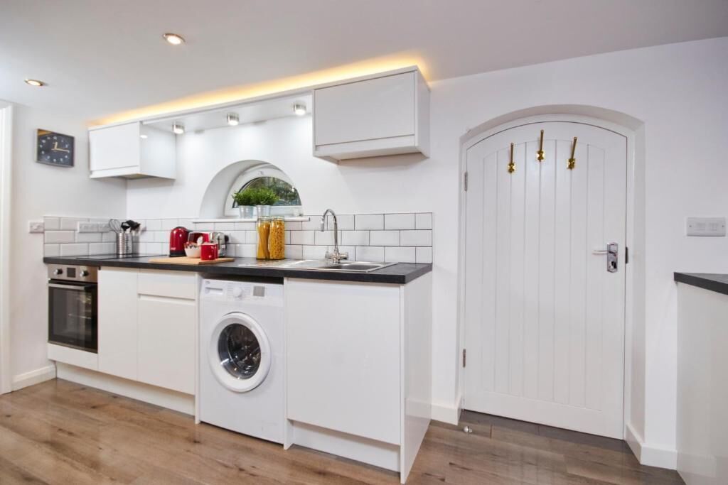 Una cocina moderna con armarios blancos, lavadora, lavaplatos y un reloj en la pared.