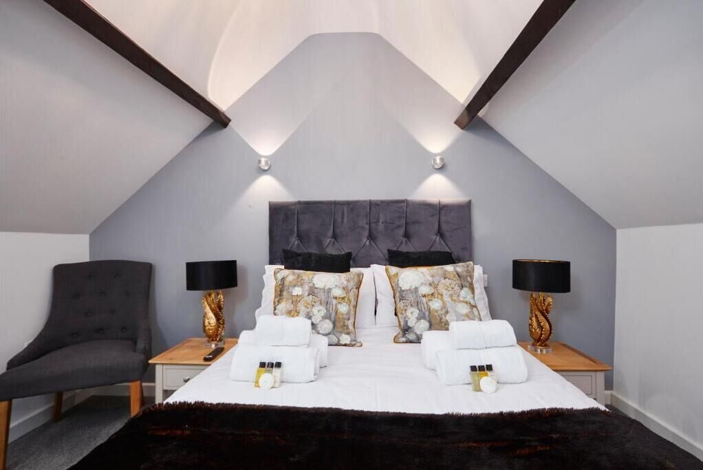 Ein modernes Schlafzimmer mit einem gesteppten Kopfteil, zwei Nachttischen mit Lampen, einem grauen Sessel und einem großen Bett mit weißen Bettwäsche und dekorativen Kissen.