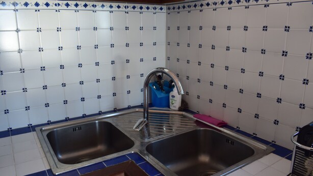 Une cuisine dotée de deux éviers en acier inoxydable, de carreaux bleus et blancs à motifs, et d’un égouttoir bleu.