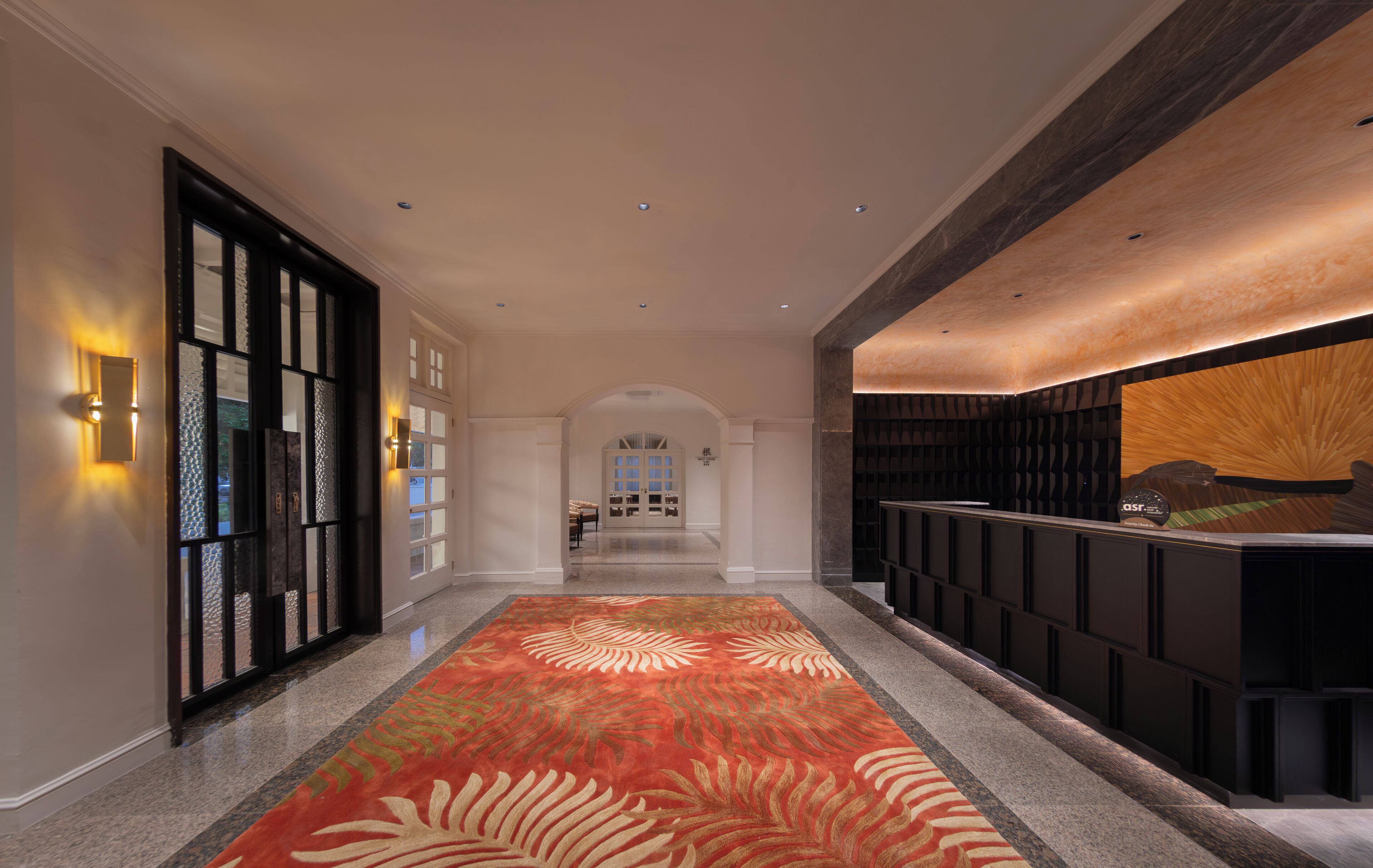A hotel lobby with a patterned carpet, a reception desk, and a view of the lobby area.