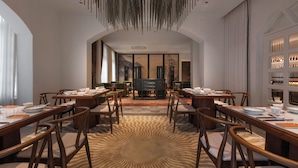 Un comedor con varias mesas y sillas, una alfombra estampada y una lámpara colgante.