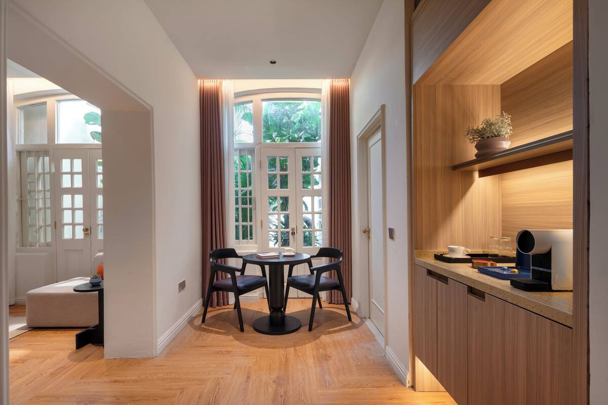 Un comedor con una mesa redonda, sillas y vistas a través de una ventana con cortinas.