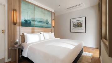 A hotel room with a large bed, a painting on the wall, a framed picture, and a small table with a plant.