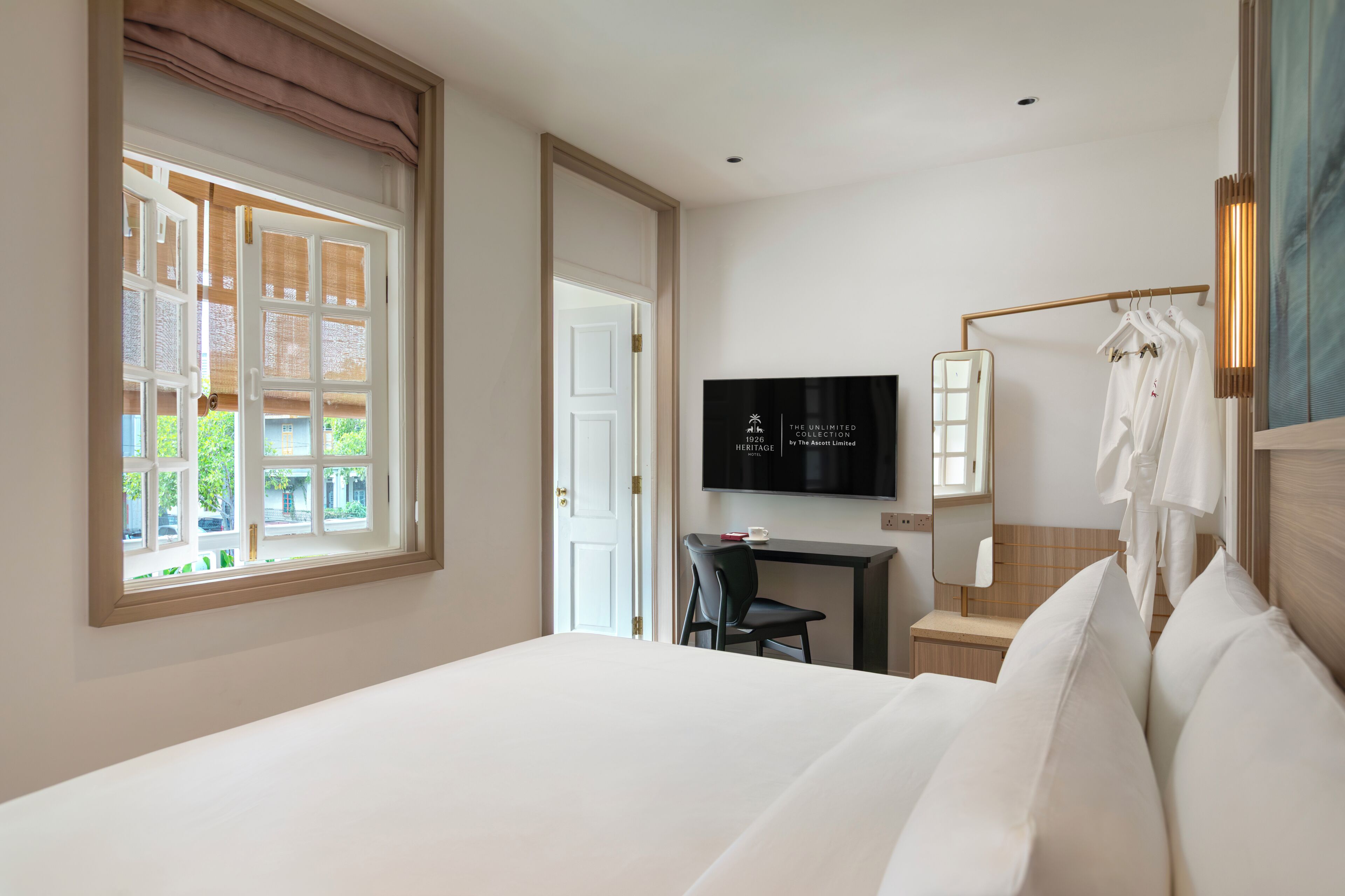 A hotel room with a bed, a desk with a chair, a TV, and a window with curtains.
