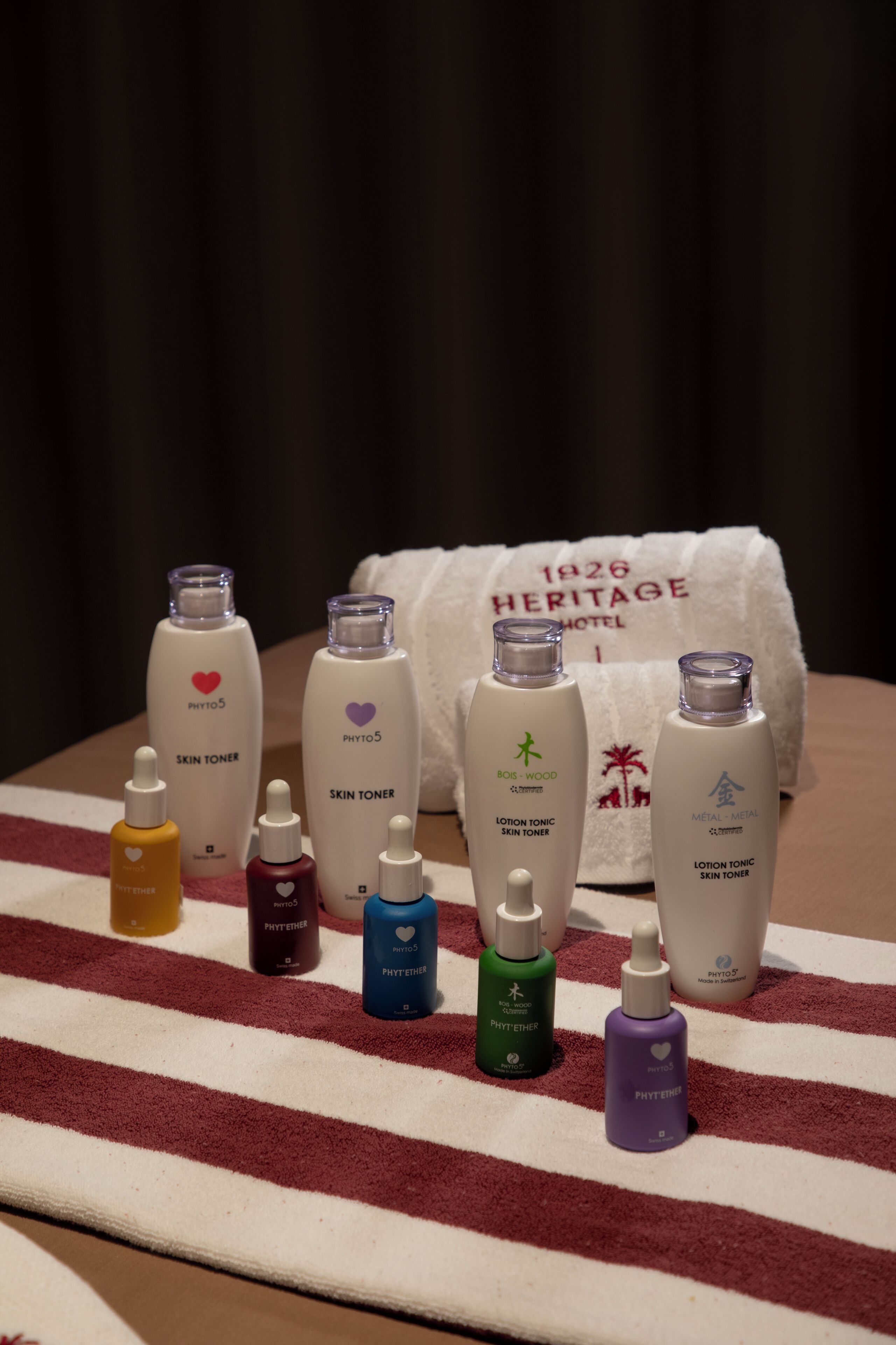 A variety of skincare products arranged on a striped towel with a white towel in the background.