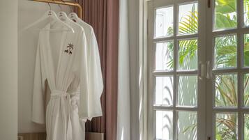 Una habitación de hotel con una cama, un ventanal con cortinas y un perchero con batas.