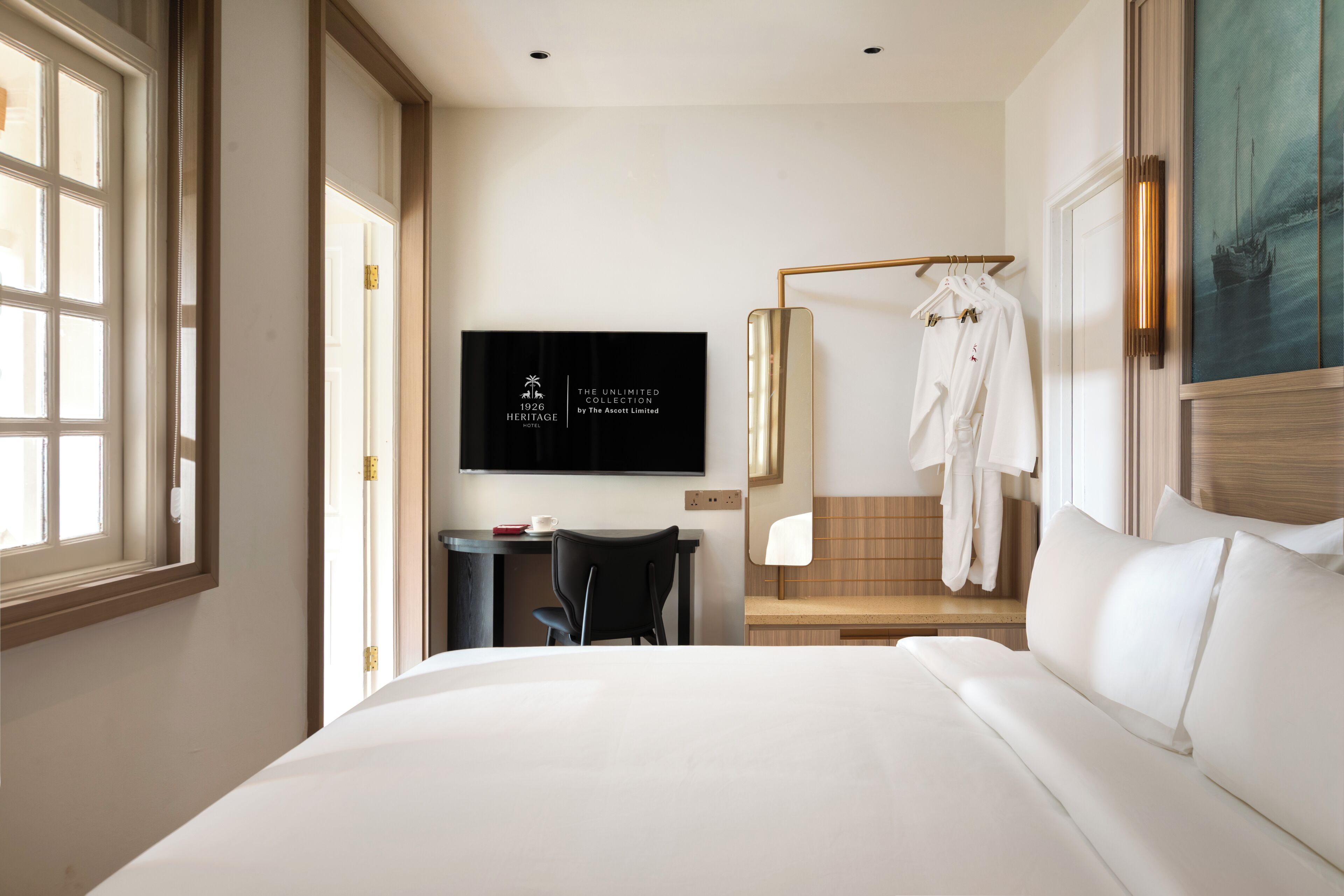 A hotel room with a bed, a desk with a chair, a TV mounted on the wall, and a robe hanging on a rack.