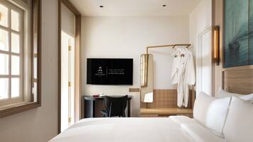 A hotel room with a bed, a desk with a chair, a TV mounted on the wall, and a robe hanging on a rack.