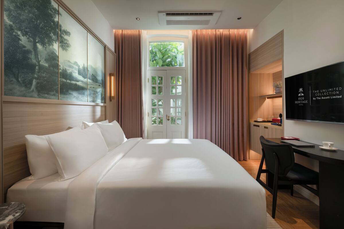 Habitación de hotel con una cama grande, un escritorio, televisión y vista a zonas verdes a través de una puerta.