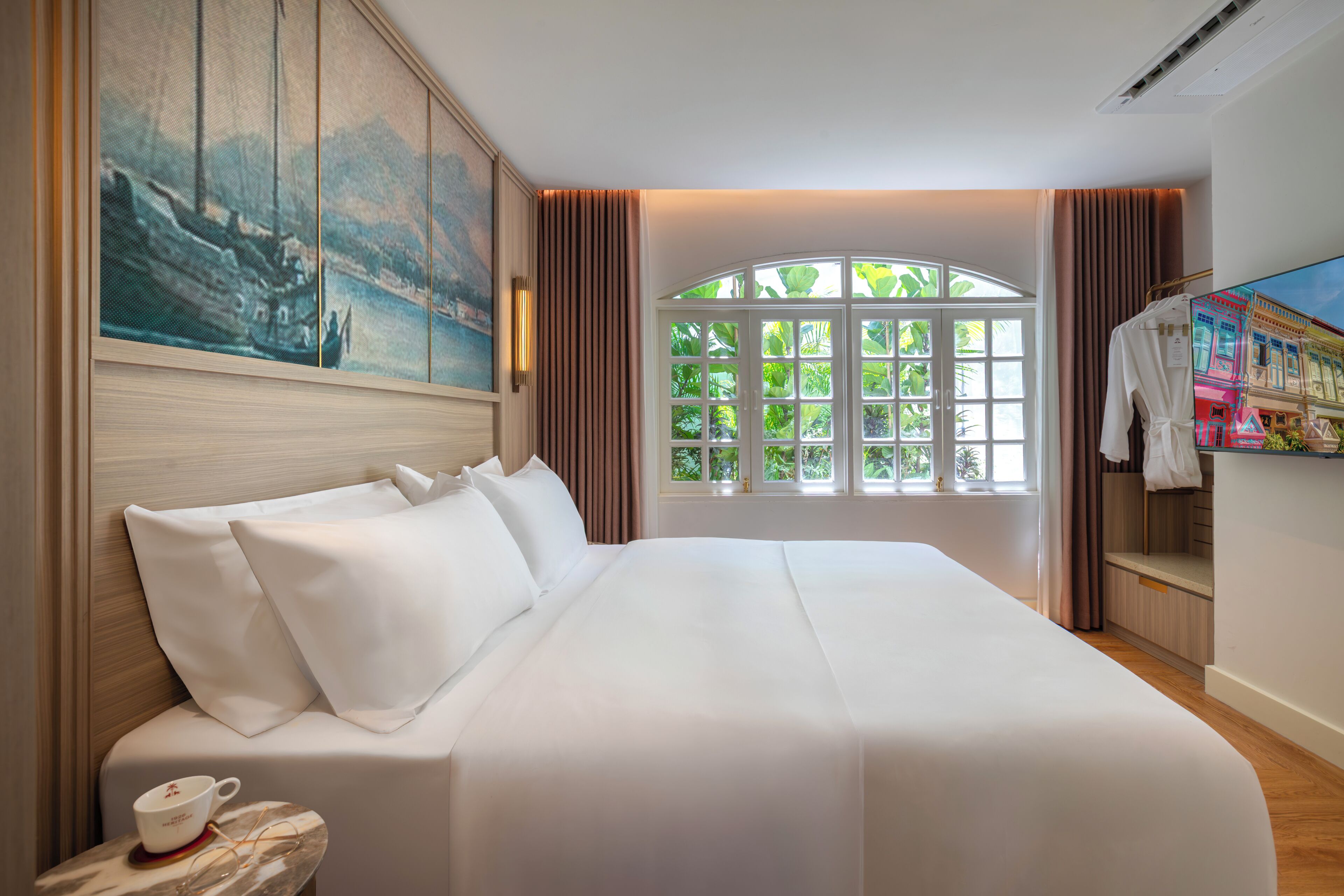 A hotel room with a large bed, a painting on the wall, a window with curtains, and a coat rack.