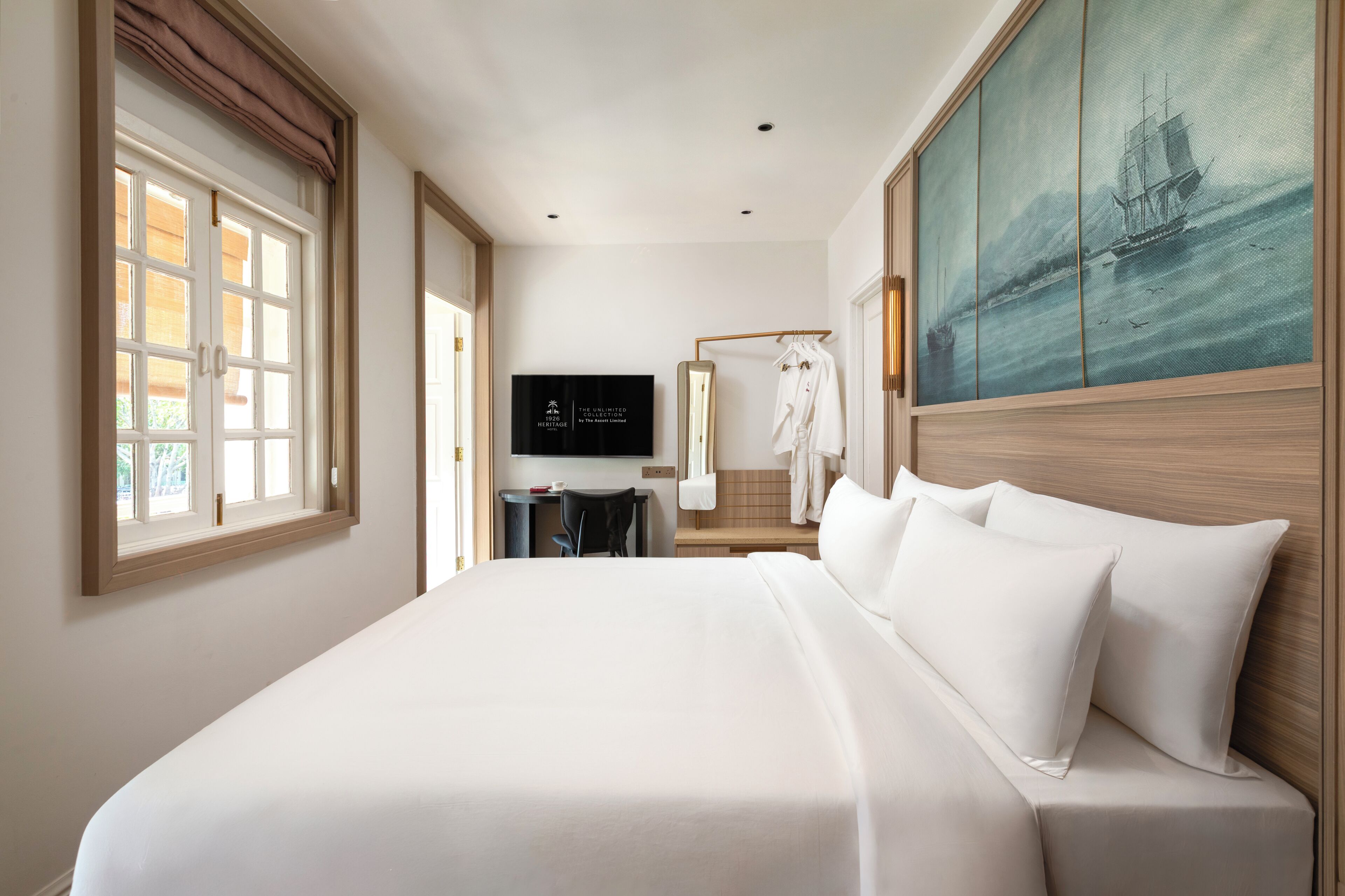 A hotel room with a large bed, a desk with a chair, a television, and a painting on the wall.