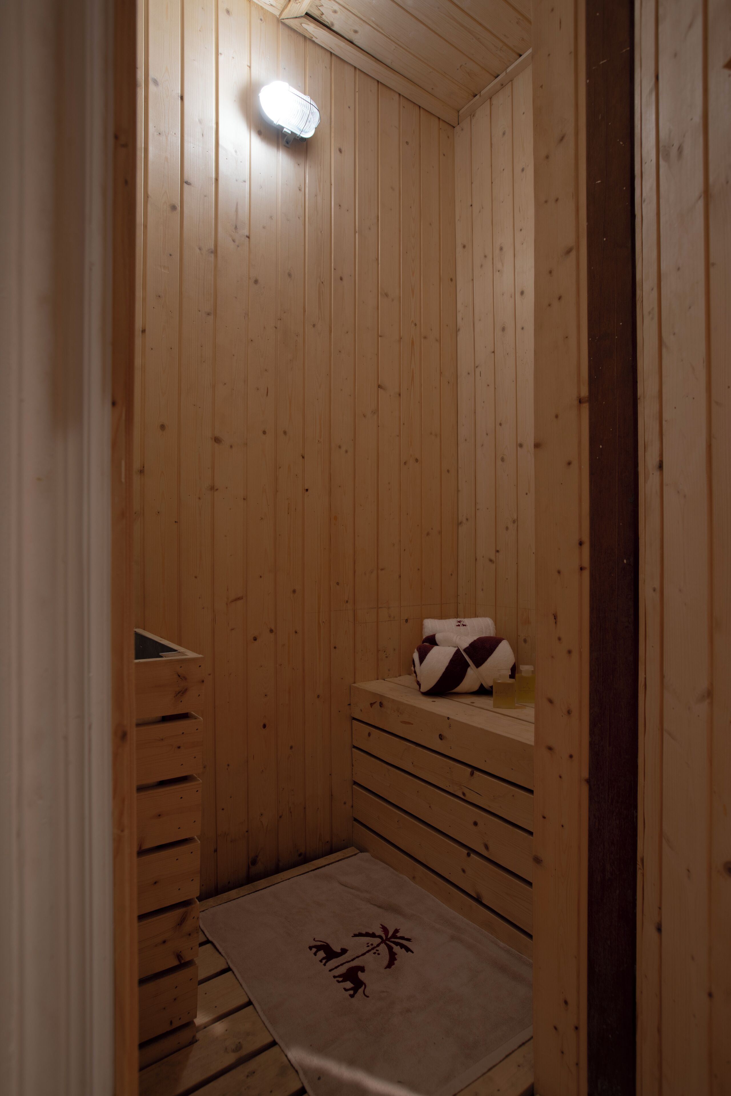 A wooden sauna room with a bench, a towel, and a light fixture.