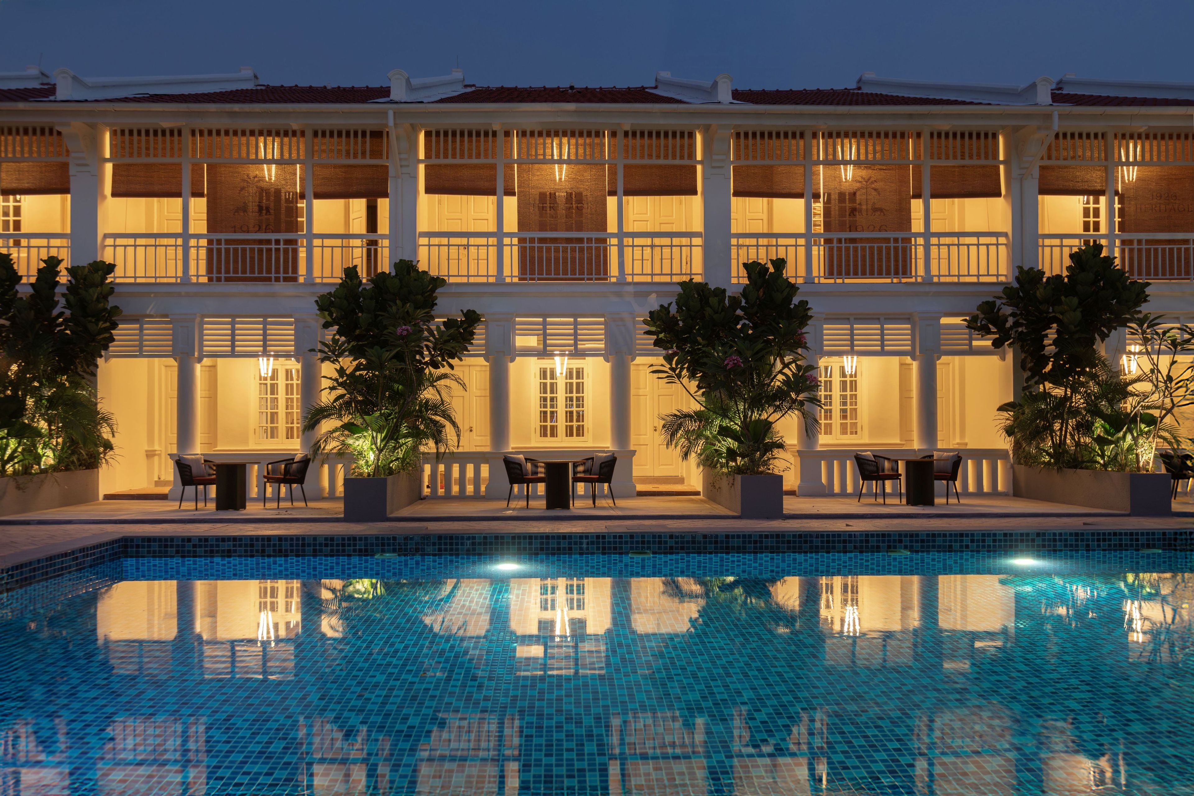 A hotel with a swimming pool, outdoor seating, and a large building with multiple windows.