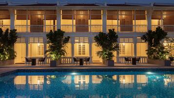 A hotel with a swimming pool, outdoor seating, and a large building with multiple windows.