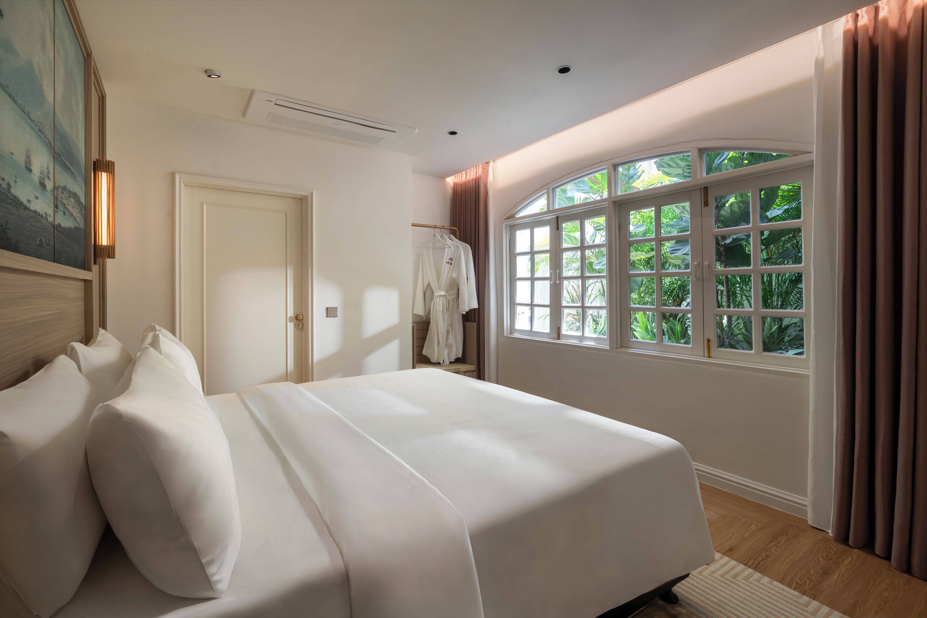 A bedroom with a large bed, a window with curtains, a door, and a painting on the wall.