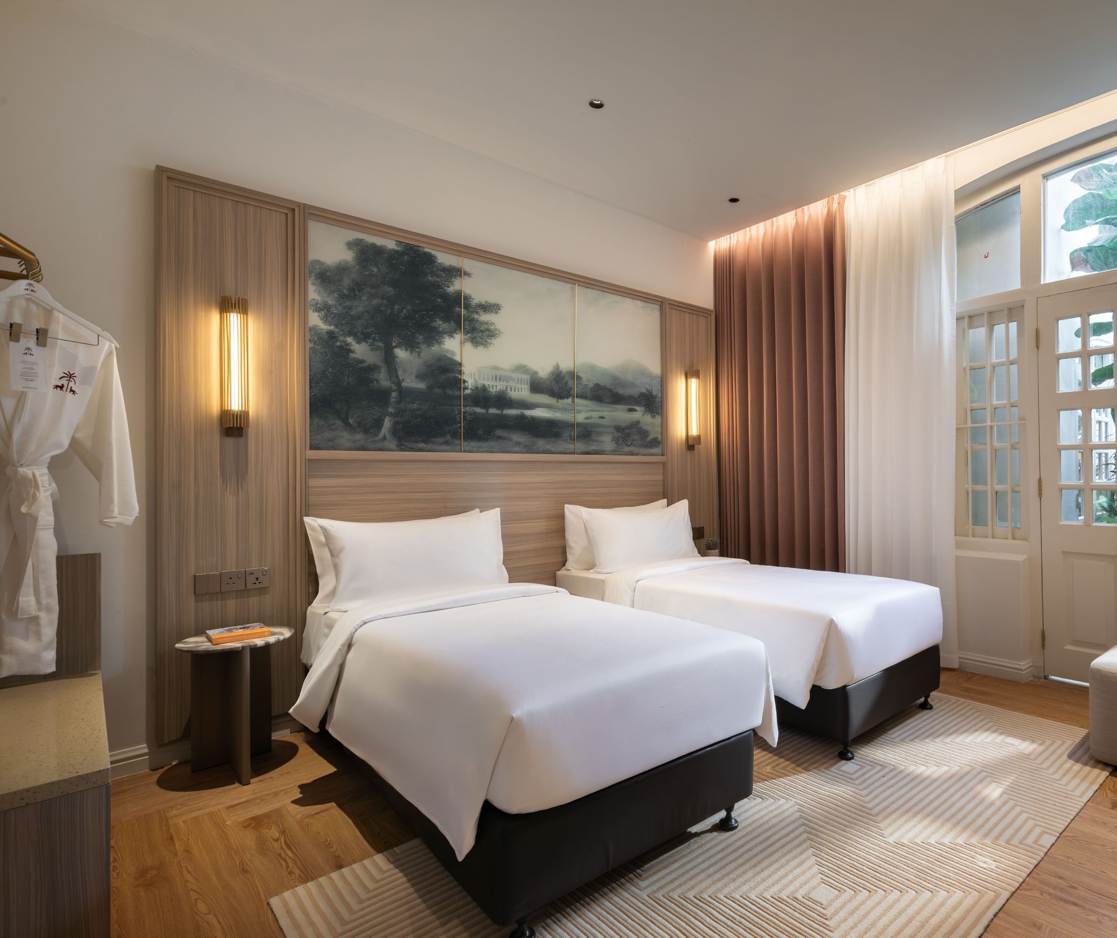 A hotel room with two beds, a large painting on the wall, a robe rack, and a window with curtains.