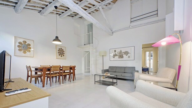 A spacious living area with a dining table, chairs, a sofa, and a coffee table. There is a staircase leading to an upper level, and artwork is displayed on the walls. - Boschetto charming apartment in Monti (Roma)