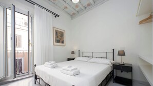 A bedroom with a bed, two bedside tables with lamps, a painting on the wall, and a balcony with a view. - Boschetto charming apartment in Monti (Roma)