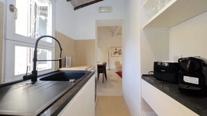 A narrow kitchen with a black sink, a window, a ceiling fan, and a black coffee maker on the countertop. - Boschetto charming apartment in Monti (Roma)