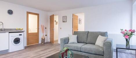 A modern living room with a grey sofa, a coffee table, a washing machine, and a radiator.