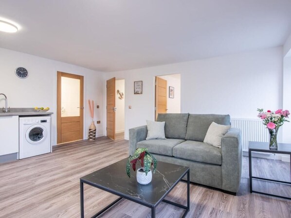 Un salon moderne avec un canapé gris, une table basse, un lave-linge et un radiateur.