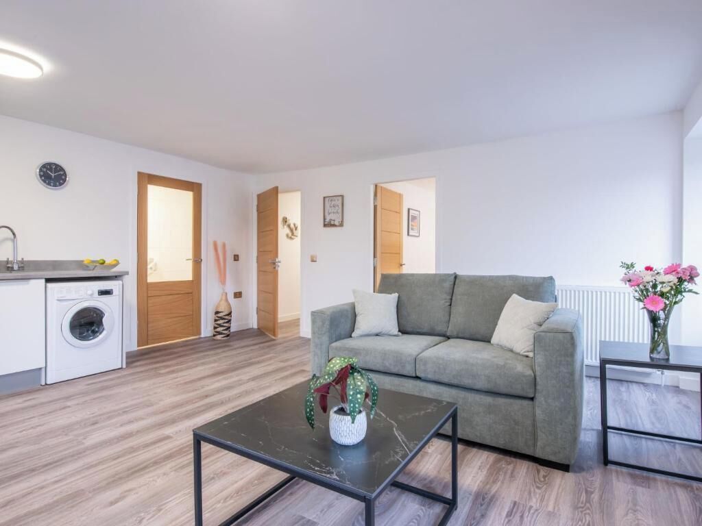 A modern living room with a grey sofa, a coffee table, a washing machine, and a radiator.