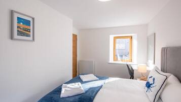 Un cuarto de hotel con cama, escritorio, silla, lámpara, ventana con vistas y un cuadro en la pared.