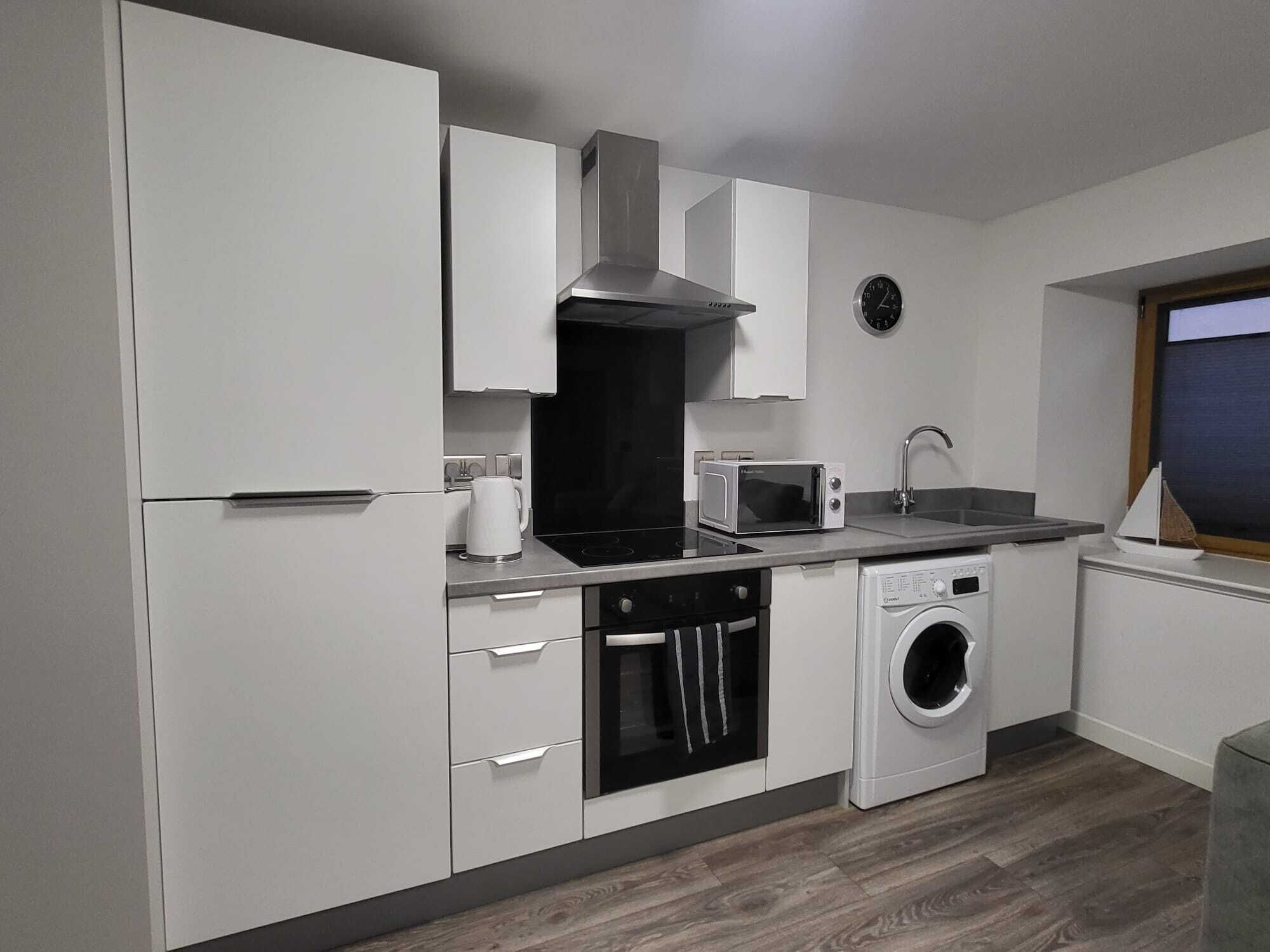 Una cocina moderna con armarios blancos, un microondas, un fregadero y una lavadora integrada.