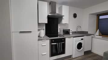 Una cocina moderna con armarios blancos, un microondas, un fregadero y una lavadora integrada.