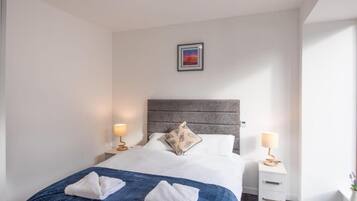 A hotel room with a bed, two bedside tables, a nightstand, a framed picture on the wall, and a window.