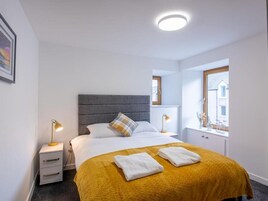 A hotel room with a bed, bedside lamps, a window, and a small table with a lamp.