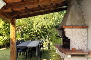 En udendørs terrasse med grill, pergola i træ og et bord med stole.