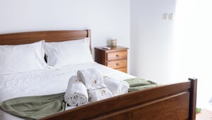 A neatly made bed with white linens and rolled towels, a wooden headboard, and a green throw blanket. - Ermal Green Haven (Vieira do Minho)