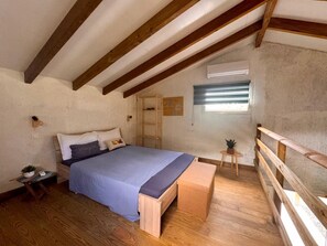 A bedroom with a wooden bed, a bench, a small table with a plant, and a window with blinds. - Air-conditioned bungalow in southern Martinique (Rivière-Salée)