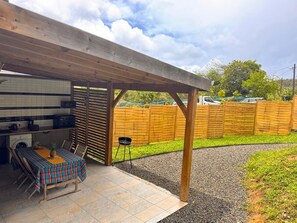 An outdoor patio area with a covered seating area, a barbecue grill, and a tiled kitchen adjacent to the patio. - Air-conditioned bungalow in southern Martinique (Rivière-Salée)
